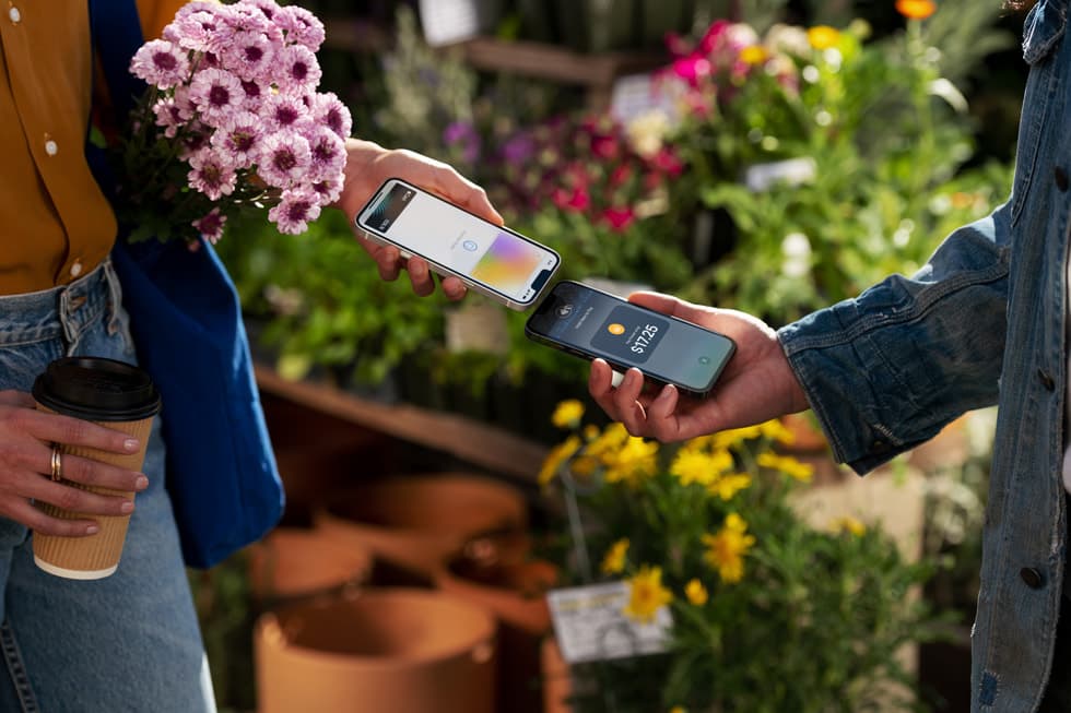 A person making an Apple Pay payment on an iPhone at a flower stall, with the payment sheet and a transaction amount showing on the screen